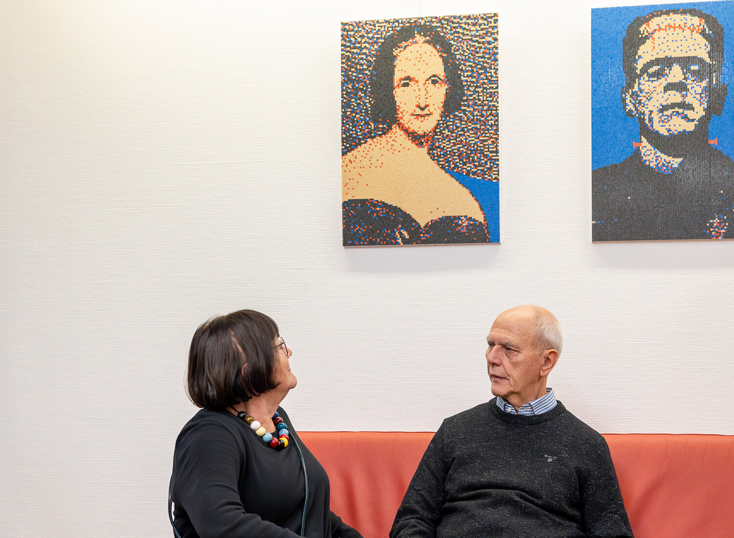 Ein Ehepaar sitzt auf einer Couch. An der Wand über ihnen hängen zwei Werke Ein Ehepaar sitzt auf einer Couch. An der Wand über ihnen hängen zwei Werke
