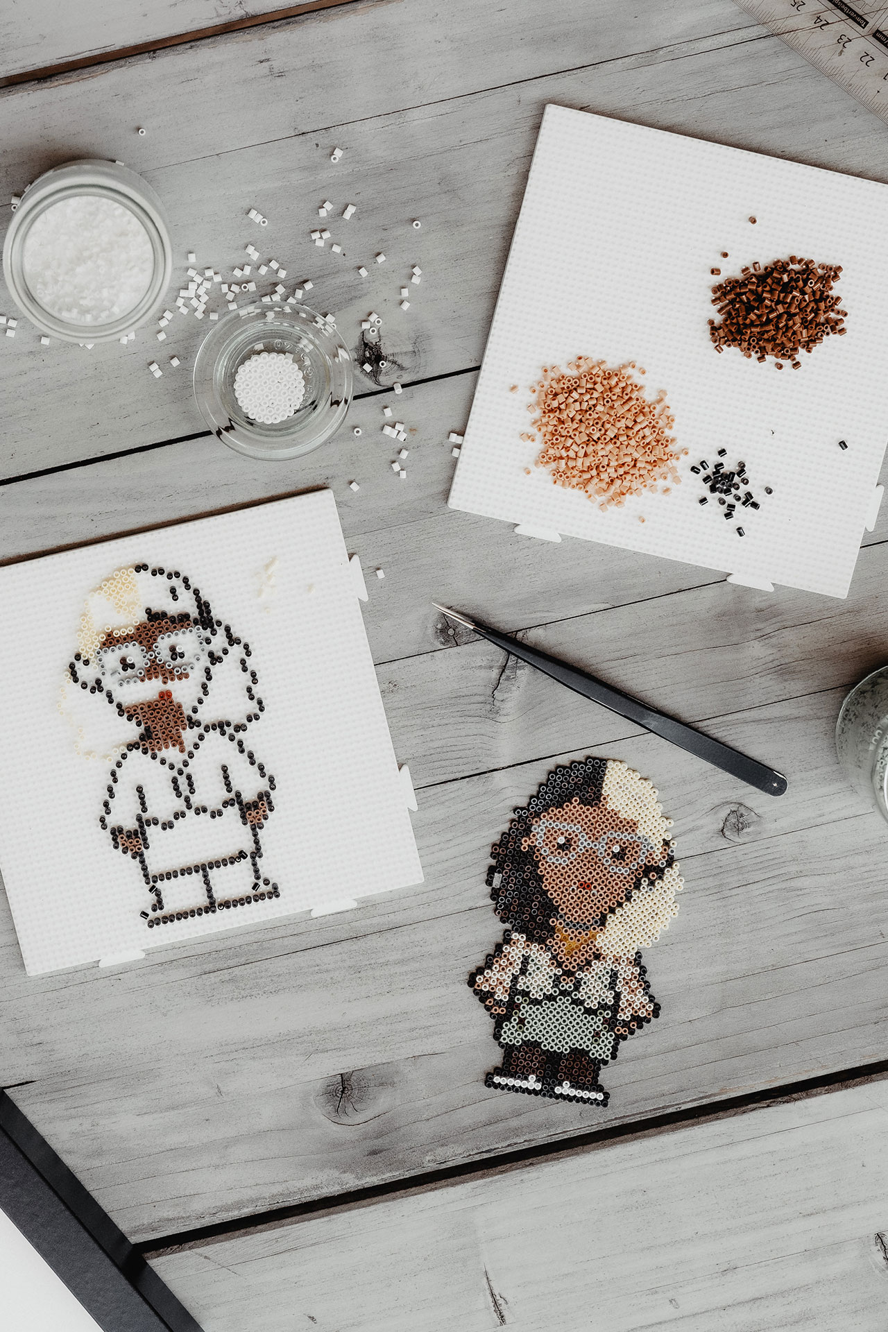Ein gedeckter Pollpixelt-Tisch mit einem Portrait aus Bügelperlen, einem angefangenen Portrait, einer Farbpalette aus Bügelperlen Ein gedeckter Pollpixelt-Tisch mit einem Portrait aus Bügelperlen, einem angefangenen Portrait, einer Farbpalette aus Bügelperlen